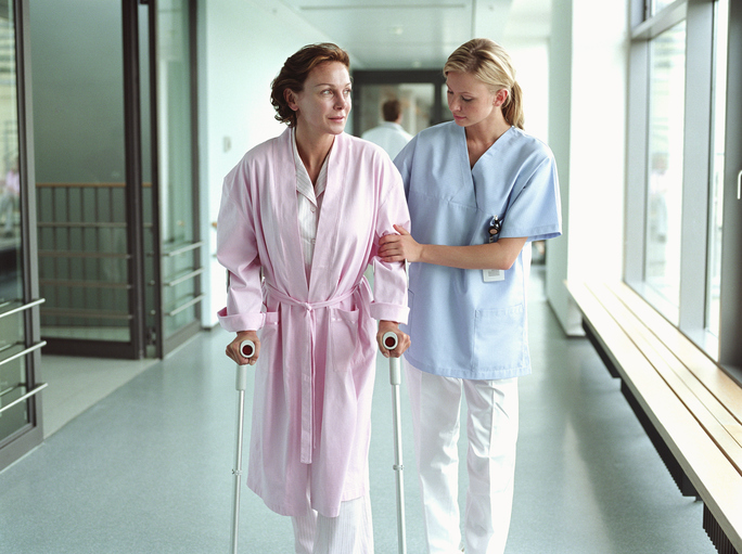 Female nurse holding patient using crutches in hospital corridor